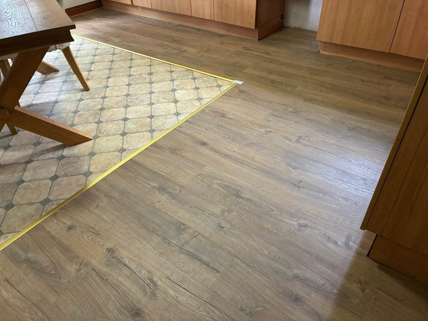 New wood-effect flooring being laid over old patterned kitchen tiles